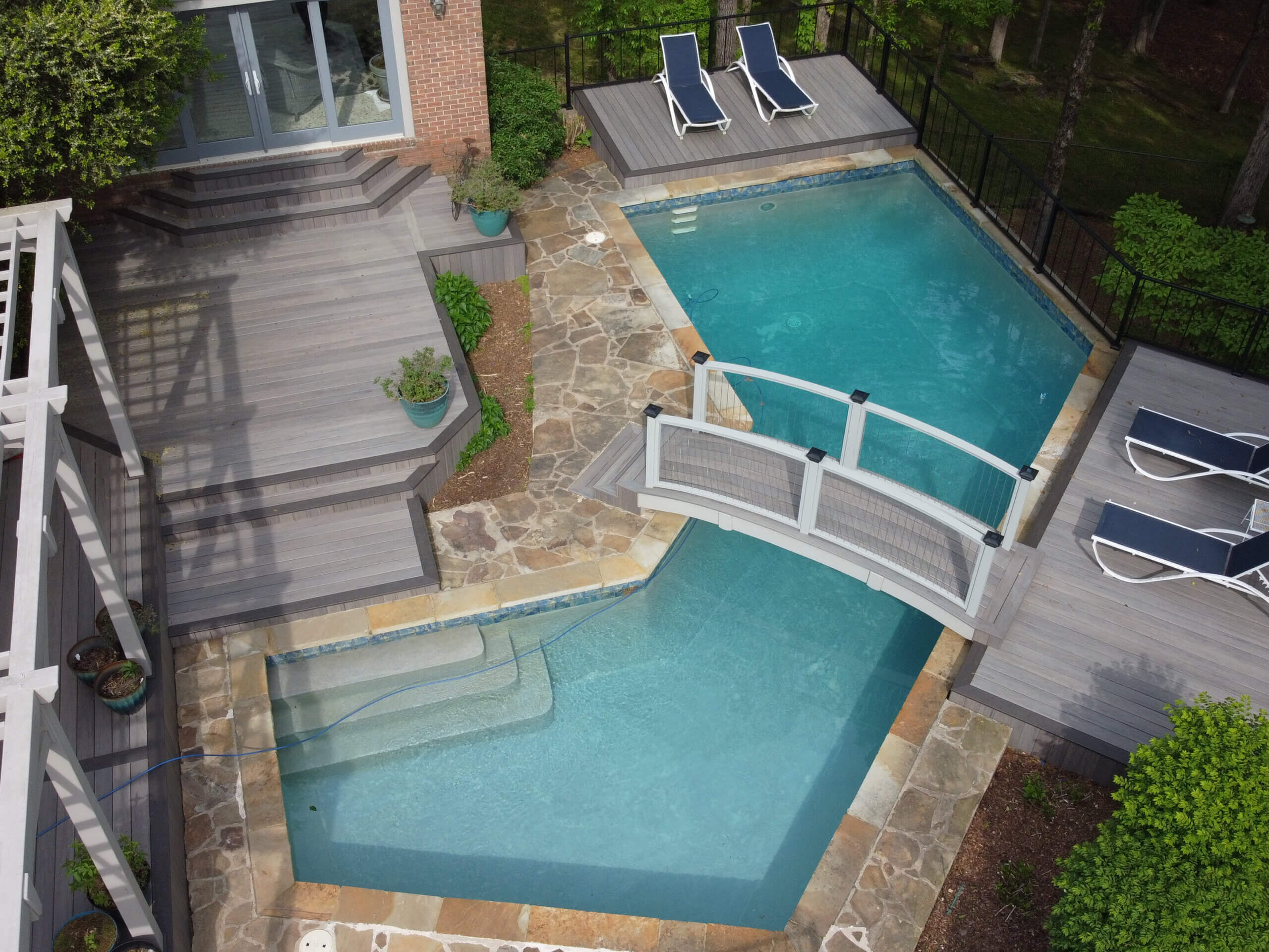 Aerial photo of new tan TimberTech deck built around a pool with a bridge over it.